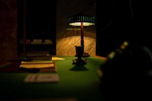 Warm Glow From a Vintage Lamp Illuminates a Dark Table Set With Books and Documents in a Quiet Study Room at Night photo