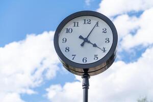 Outdoor Clock Displaying Time Against a Bright Blue Sky With Fluffy Clouds in a Public Park Setting photo