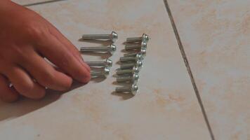 Hand Arranging Metal Screws on Tiled Floor video