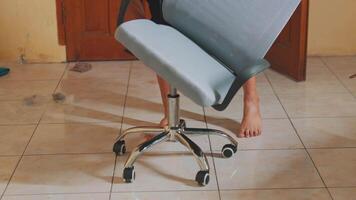 A person assembling an office chair, adjusting the seat height with hands on the chair. The setting is indoors with tiled flooring and wooden doors in the background. video