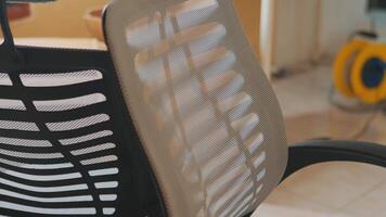A close-up view of a modern ergonomic office chair with a mesh backrest. The chair features a sleek design, showcasing the intricate patterns of the mesh material and the contrasting video
