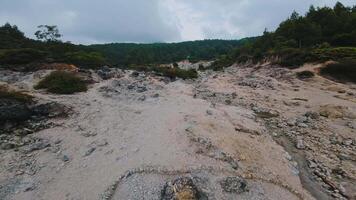 A barren landscape with rocky terrain and sparse vegetation, featuring a dry riverbed and patches of greenery in the background under a cloudy sky. video