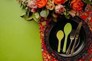 Festive Table Setting with Colorful Flowers and Modern Cutlery. A vibrant spring or summer table arrangement featuring a black charger, lime green spoons, and a bouquet of roses. photo