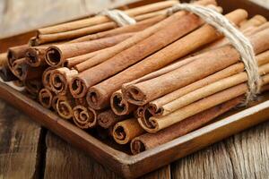 Aromatic Cinnamon Sticks Bundled in Rustic Wooden Tray. A close-up image of fragrant cinnamon sticks tied together with twine, resting on a weathered wooden surface. photo