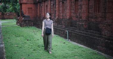 Handheld high angle view shot, Relaxed young woman wearing a striped shirt and green pants walking around, admiring the natural scenery and ancient brick structures, Enjoy holiday travel. video