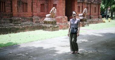 Young Asian woman wearing a striped shirt and green pants walking around, admiring the natural scenery and ancient brick structures, Enjoy holiday travel. video