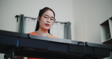Low angle view shot, Happy young woman in an orange shirt is practicing her keyboard skills intently in a living room. Enjoy favorite musical instruments video