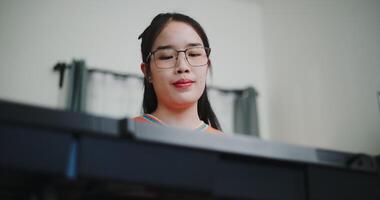 Handheld low angle view shot, Happy young woman in an orange shirt is practicing her keyboard skills intently in a living room. Enjoy favorite musical instruments video