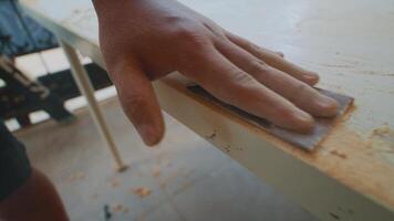 A close-up of a wooden surface being sanded, showing fine wood shavings and a smooth edge. The background is blurred, focusing on the craftsmanship of woodworking. video