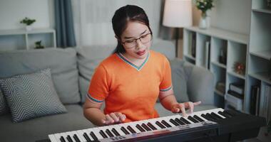 Handheld high angle view shot, Happy young woman in an orange shirt is practicing her keyboard skills intently in a living room. Enjoy favorite musical instruments video