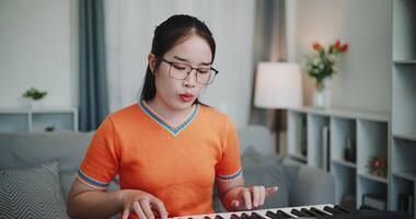 Handheld medium shot, Happy young woman in an orange shirt is practicing her keyboard skills intently in a living room. Enjoy favorite musical instruments video