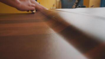 A close-up of a person's hand using a scraper on a wooden surface, showcasing craftsmanship and attention to detail in woodworking. video