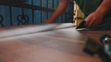 A close-up of a hand using a tool to smooth a wooden surface, showcasing craftsmanship and attention to detail. The background features a decorative railing. video