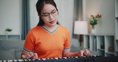 young woman in an orange shirt is practicing her keyboard skills intently in a living room. Enjoy favorite musical instruments video