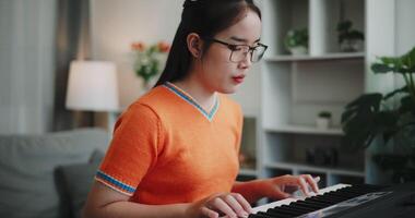 Handheld shot, Happy woman in an orange shirt is practicing her keyboard skills intently in a living room. Enjoy favorite musical instruments video