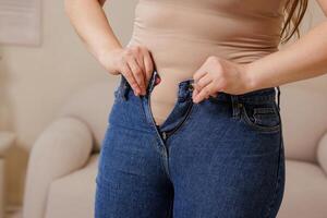 Close Up of Woman Struggling to Button Tight Jeans Weight Loss Diet Body Image and Motivation Concept photo