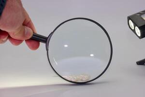 Hand holding magnifying glass over small white objects in a well lit workspace with a spotlight on the table photo