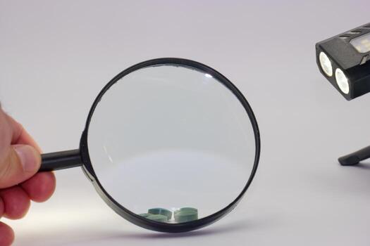Magnifying glass held by a person near a light source and small objects on a surface in a well lit environment photo