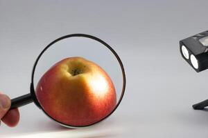 Examining a shiny red apple with a magnifying glass under bright light in a controlled environment photo