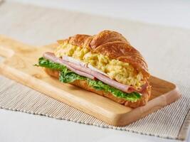 Scrambled Egg, Brie Cheese and Ham Croissant with lettuce on wooden board side view of breakfast menus photo