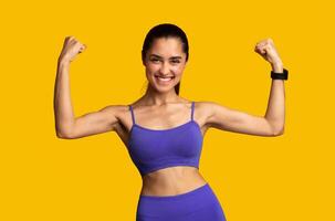 Yes, I Did It. Portrait of happy emotional young sporty lady in sportswear celebrating win and success, shaking and raising clenched fists in the air isolated over orange studio background photo