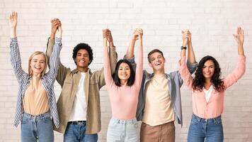 Teamwork, support from friend in studies and emotions of success. Cheerful digital young international people hold hands and lift up and have fun, on white wall background, studio shot, empty space photo