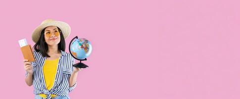 Dream Vacation. Portrait of excited happy asian woman traveller holding passport with plane boarding pass tickets and globe, wearing sunglasses, looking up and dreaming about trip, pink studio wall photo