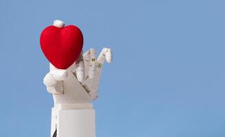 Future of healthcare and medicine. Automated hand of robot doctor holding red heart on blue background with copy space photo