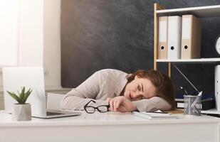 Tired middle aged businesswoman sleeping on her workplace while working on laptop in office photo