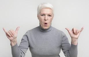 Cool grandmother showing modern trendy rock gesture on light studio background, copy space photo