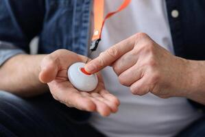 Unrecognizable senior man pushing panic button on emergency equipment for elderly people, cropped. Closeup of man's hand pressing alarm button for emergency hung on his chest photo