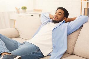 Finally weekend Young african-american man relaxing at home, having rest on sofa at home, copy space photo
