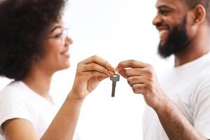 Joyful Black Couple Holding New House Key Smiling Each Other Standing Posing Over White Background Indoors, Selective Focus On Keys. Apartment Ownership, Real Estate And Family Housing Concept photo