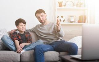 Happy father and son watching a movie on a laptop, sitting on a sofa at home photo