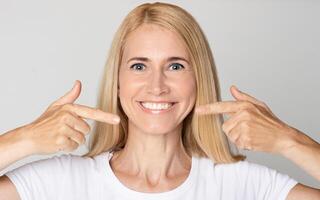 Strong healthy teeth. Woman pointing on her perfect smile over grey studio background photo