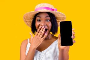 Online sale. Emotional black lady showing cellphone with empty screen, covering mouth in shock on orange studio background, mockup for mobile app or website. Selective focus photo