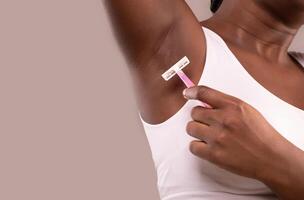 Hair Removal. Unrecognizable Black Woman Shaving Her Armpit With Pink Razor, African American Female Making Underarm Depilation, Standing Isolated Over Grey Background, Closeup, Copy Space photo