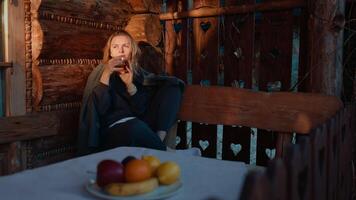 Sunlight streams across weathered wooden logs as woman enjoys steaming mug while relaxing inside cozy mountain cabin during tranquil morning pause. Woman drinks hot beverage, sitting rustic cabin video