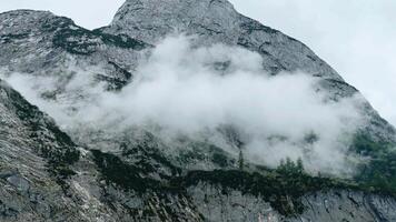 Clouds roll through rocky mountains revealing lush greenery and rugged terrain in nature's breathtaking landscape video