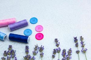 Colorful sewing threads and buttons arranged with fresh lavender on a light surface photo