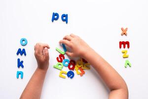 Child arranging colorful alphabet magnets on white background photo