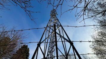A striking and captivating view of a large communication tower secured tightly by barbed wire against a clear blue sky photo