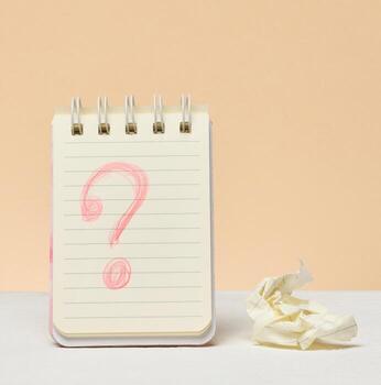 An open notebook with a question mark drawn in red pencil next to a crumpled piece of paper. photo