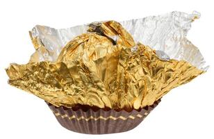 Empty golden foil wrapper from round candy, partially unfolded and placed in brown paper form, isolated on background. photo