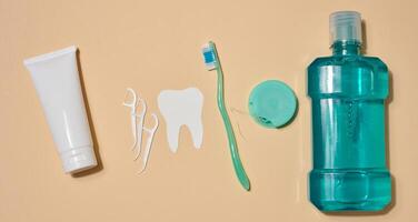 Oral hygiene set including a tube of toothpaste, a toothbrush, dental floss and a bottle of mouthwash, beige background. Top view. photo