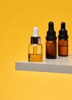 Cosmetic bottles with pipettes on a stone stand. Stylish composition for skin care, oils and serums on a bright yellow background. photo