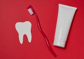 Red toothbrush, white tube of toothpaste and white paper tooth cut out on red background. photo