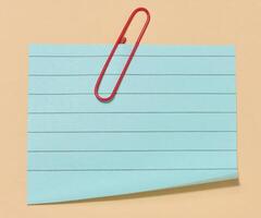 Blue sticky note with a red paper clip attached to it, placed on a beige background. Top view photo
