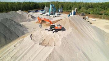 The equator works with a bucket on a pile of sand and gravel, aerial view. Crawler bulldozer pushes sand. Asphalt concrete plant. Republic of Bashkortostan, Ufa, August 18, 2023 video