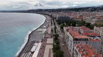 Aerial view of the Promenade des Anglais in Nice, France, featuring a pebble beach, turquoise Mediterranean waters, palm-lined streets, and vibrant city buildings. June 2nd, 2024. Nice, France video